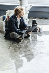 Businessman sitting on floor with laptop and paint buckets - KNSF00974