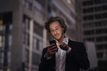 Businessman in the city at dusk using cell phone - KNSF00991