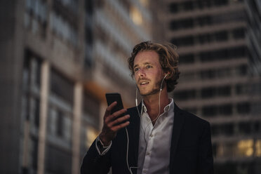 Businessman in the city at dusk using cell phone - KNSF00993