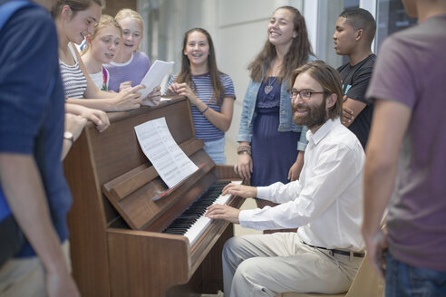 Lehrer mit einer Gruppe von Schülern, die um ein Klavier herumstehen - ZEF12664