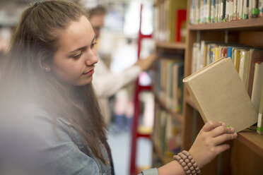 Studentin in der Bibliothek, die ein Buch zurück ins Regal stellt - ZEF12667