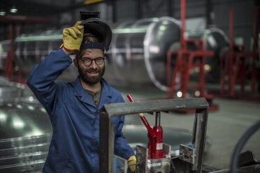 Porträt eines lächelnden Mannes mit einer Schweißermaske in einer Fabrik - ZEF12688