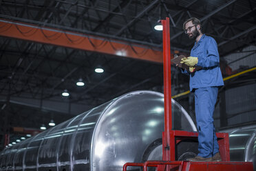 Man with clipboard inspecting steel tank in factory - ZEF12690