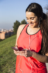 Smiling female athlete with earphones using her phone - ABZF01836