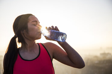 Weibliche Athletin trinkt Wasser bei Sonnenuntergang - ABZF01846