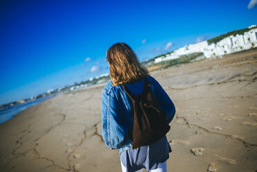 Spain, Conil de la Frontera, back view of young woman strolling on the beach - KIJF01168