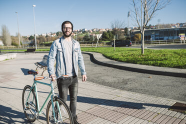 Young man walking with his fixie bike in a park - RAEF01719