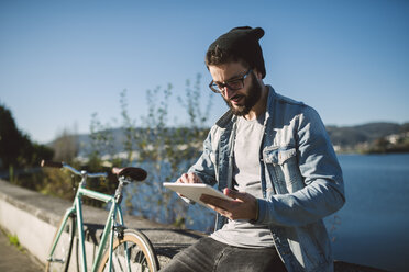 Smiling young man using a tablet at the waterfront - RAEF01720