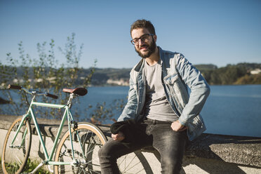 Lächelnder junger Mann mit seinem Fixie-Fahrrad an der Waterfront - RAEF01722