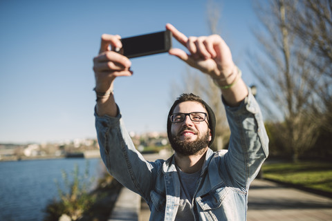 Ein lächelnder junger Mann macht ein Selfie am Wasser, lizenzfreies Stockfoto