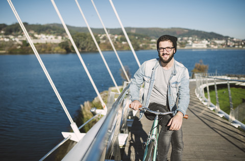 Lächelnder junger Mann mit seinem Fixie-Fahrrad auf einer Brücke, lizenzfreies Stockfoto