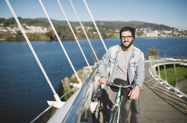 Smiling young man with his fixie bike on a bridge - RAEF01726