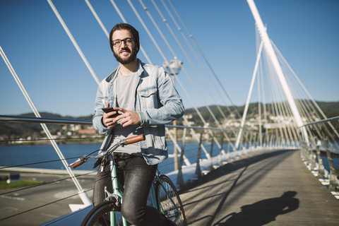 Lächelnder junger Mann mit Fixie-Fahrrad auf einer Brücke, lizenzfreies Stockfoto