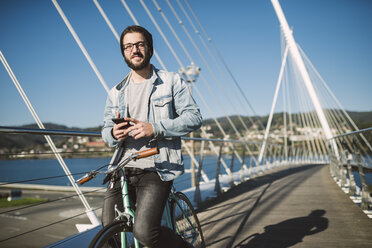 Lächelnder junger Mann mit Fixie-Fahrrad auf einer Brücke - RAEF01727