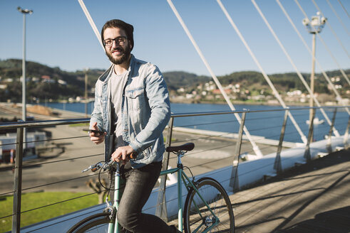Smiling young man with fixie bike on a bridge - RAEF01730