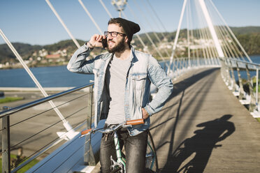 Junger Mann mit Fixie-Fahrrad auf einer Brücke beim Telefonieren - RAEF01731