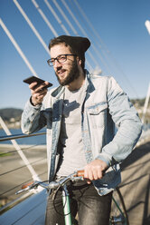 Young man with fixie bike on a bridge using smartphone - RAEF01733