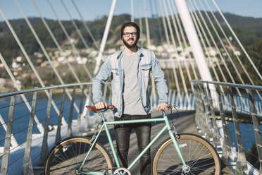 Lächelnder junger Mann mit seinem Fixie-Fahrrad auf einer Brücke - RAEF01735