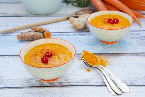 Zwei Schalen Karotten-Kurkuma-Suppe mit Ingwer und Chili und Zutaten, lizenzfreies Stockfoto