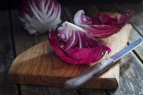 Leaves of radicchio and kitchen knife on wooden board - YFF00631