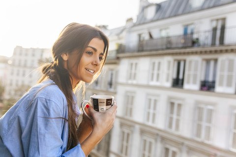 Young woman standing on balcony, holding cup of coffee stock photo