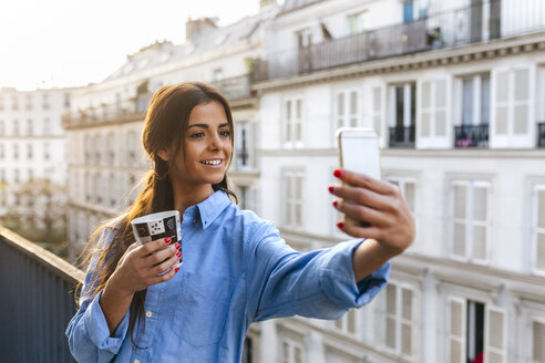 Junge Frau steht auf einem Balkon und macht ein Selfie mit ihrem Smartphone - MGOF02869