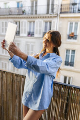 Junge Frau steht auf einem Balkon und macht ein Selfie mit einem digitalen Tablet - MGOF02870