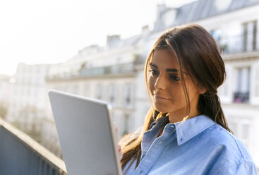 Junge Frau steht auf einem Balkon und benutzt ein digitales Tablet - MGOF02871