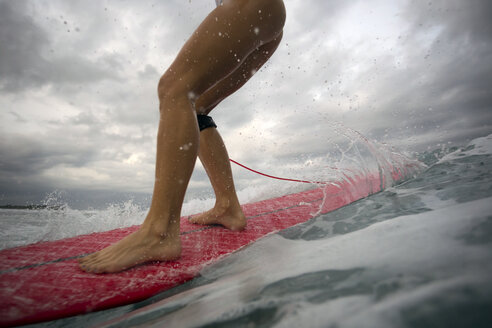 Indonesien, Bali, Beine einer Frau auf einem Surfbrett - KNTF00632