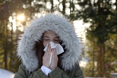Teenage girl wearing hooded jacket blowing her nose in winter - LBF01548