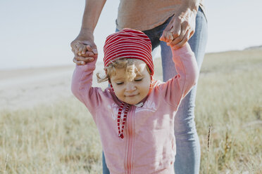 Lächelndes Kleinkind hält die Hände seiner Mutter auf einer Wiese - DWF00271