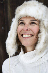 Porträt einer lächelnden Frau mit Pelzmütze im Winter, die nach oben schaut - FSF00730