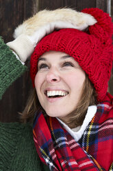 Porträt einer lächelnden Frau mit roter Bommelmütze und Pelzhandschuhen im Winter - FSF00735