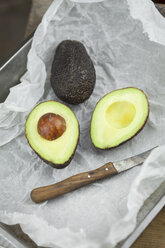 Whole and sliced avocado and kitchen knife on parchment paper - JUNF00814