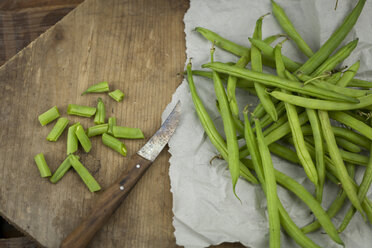 Whole and chopped green beans and kitchen knife on paper and wooden board - JUNF00825