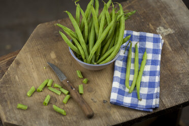 Whole and chopped green beans, cloth and kitchen knife on wooden board - JUNF00826