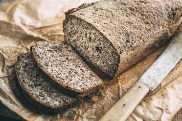 Selbstgebackenes glutenfreies Vollkornbrot und Brotmesser auf braunem Papier - IPF00354