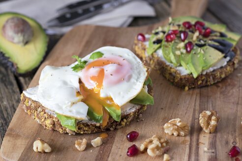 Eiweißbrotscheibe mit Frischkäse, Avocadoscheiben und Spiegelei auf Holzbrett - YFF00637