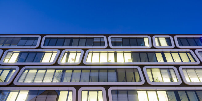 Teil der Fassade eines beleuchteten Bürogebäudes am Abend - WDF03864