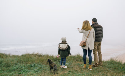 Family with dog at the coast on a foggy winter day looking at view - DAPF00555