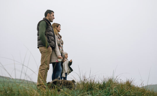 Family with dog standing on a meadow on a foggy winter day - DAPF00557