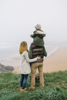 Family with dog at the coast on a foggy winter day looking at view - DAPF00558