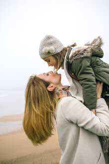 Woman lifting up and kissing daughter on the beach in winter - DAPF00559