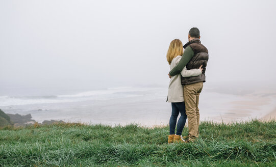 Couple hugging at the coast on a foggy winter day looking at view - DAPF00560