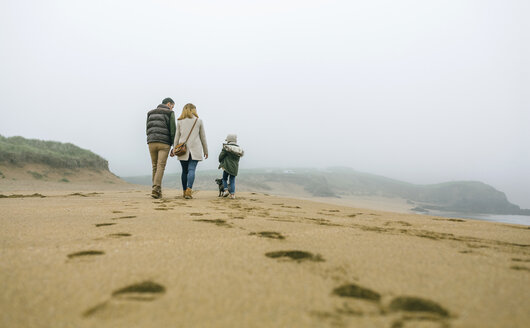 Family walking with dog on the beach on a foggy winter day - DAPF00562