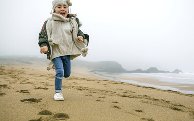 Glückliches Mädchen, das an einem nebligen Wintertag am Strand läuft - DAPF00565