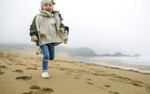 Happy girl running on the beach on a foggy winter day - DAPF00565