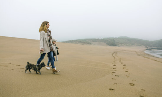 Frau, die an einem nebligen Wintertag mit Tochter und Hund am Strand spazieren geht - DAPF00567