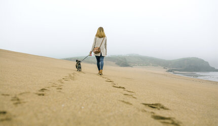 Frau geht mit Hund am Strand im Winter spazieren - DAPF00568