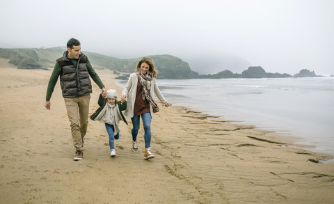 Happy family with daughter walking on the beach in winter stock photo